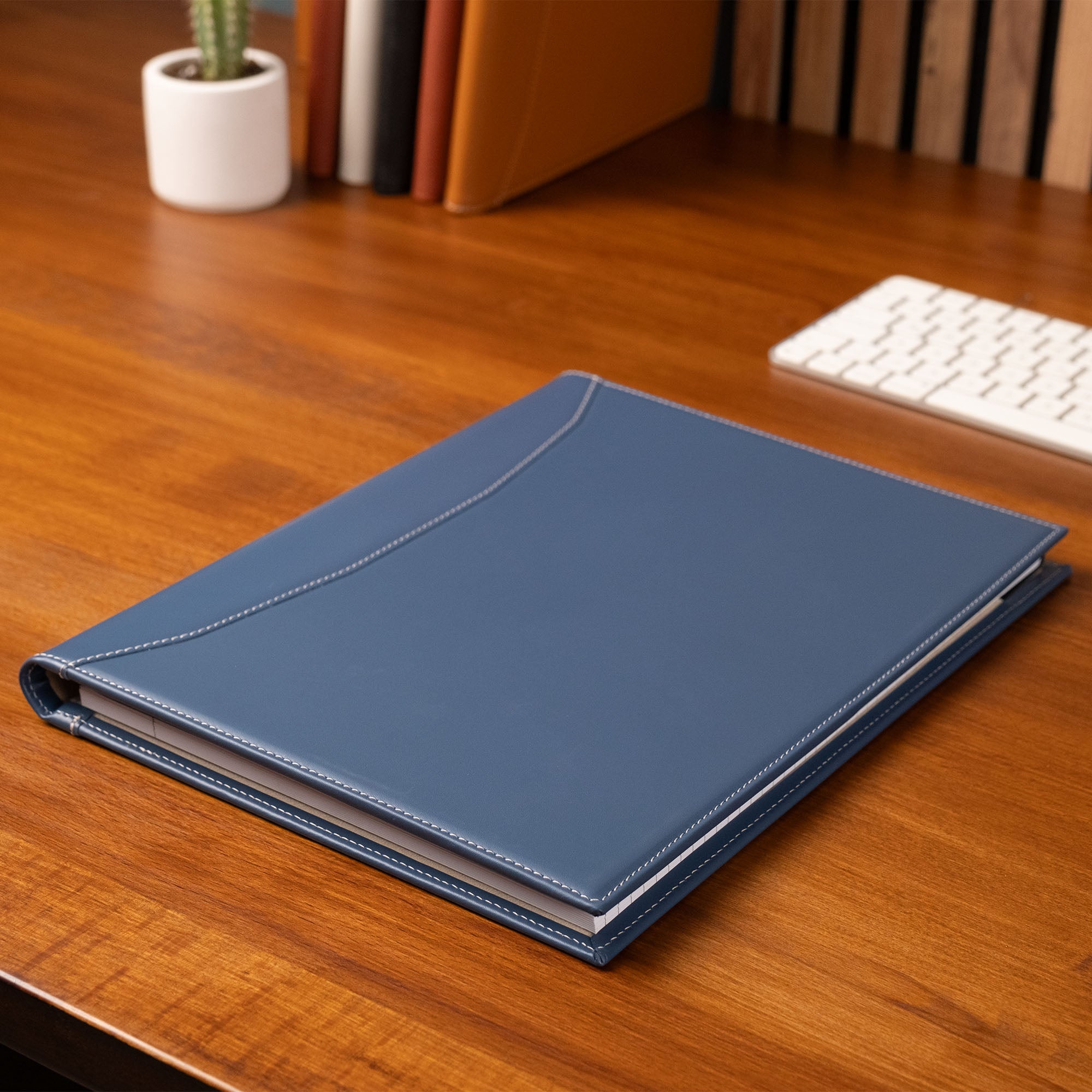 Blue notebook on a wooden desk with books and a keyboard in the background