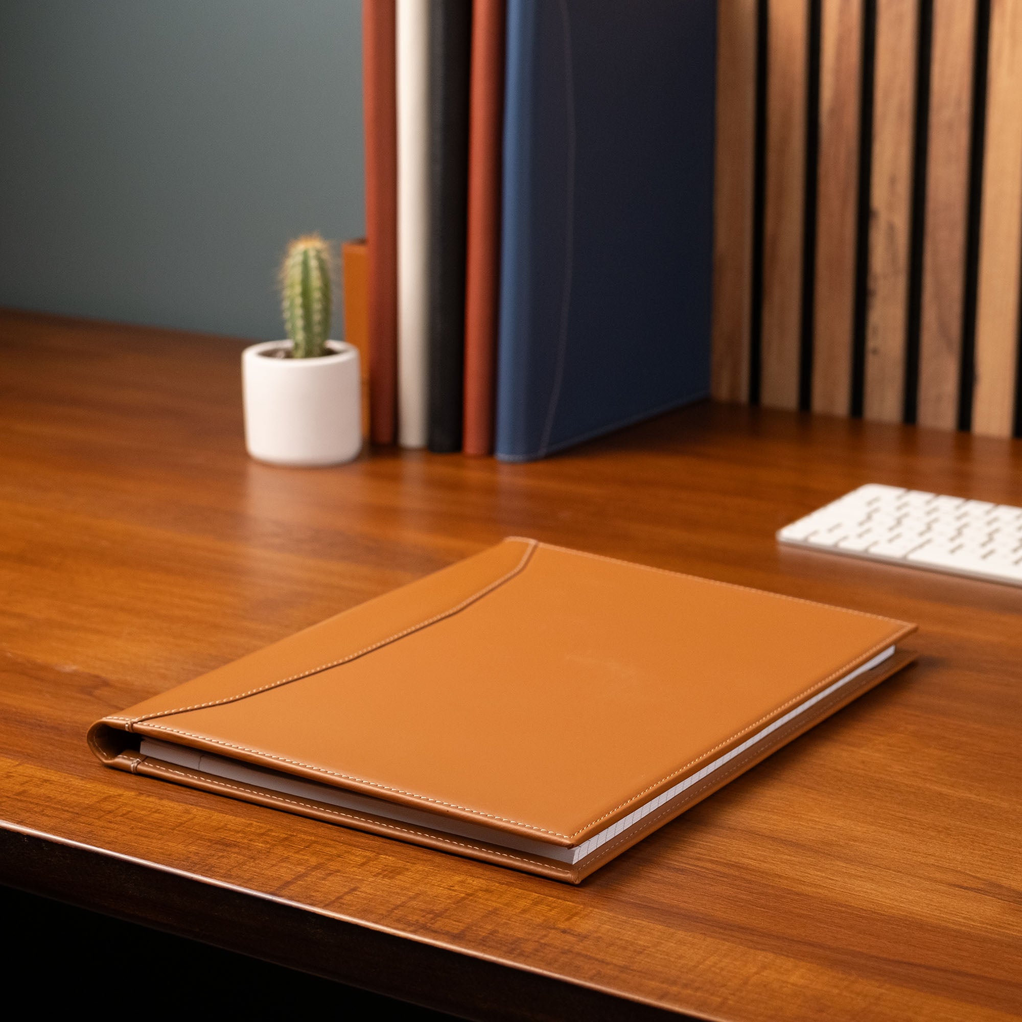 Brown leather notebook on a wooden desk with books and a keyboard in the background