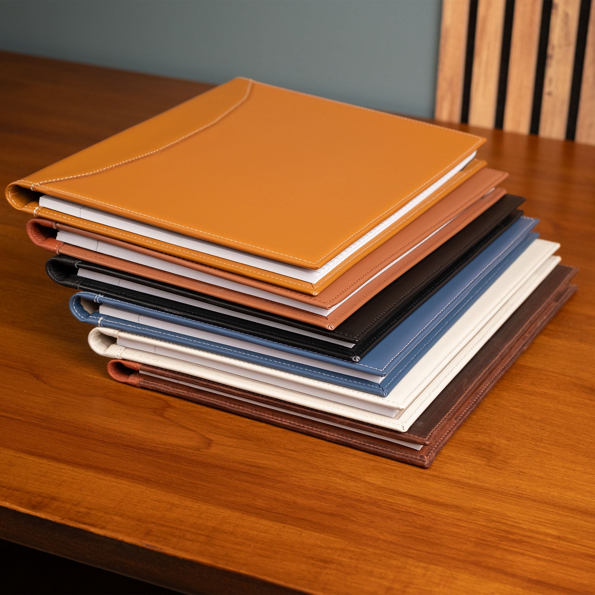 Stack of leather-bound notebooks in various colors on a wooden surface.