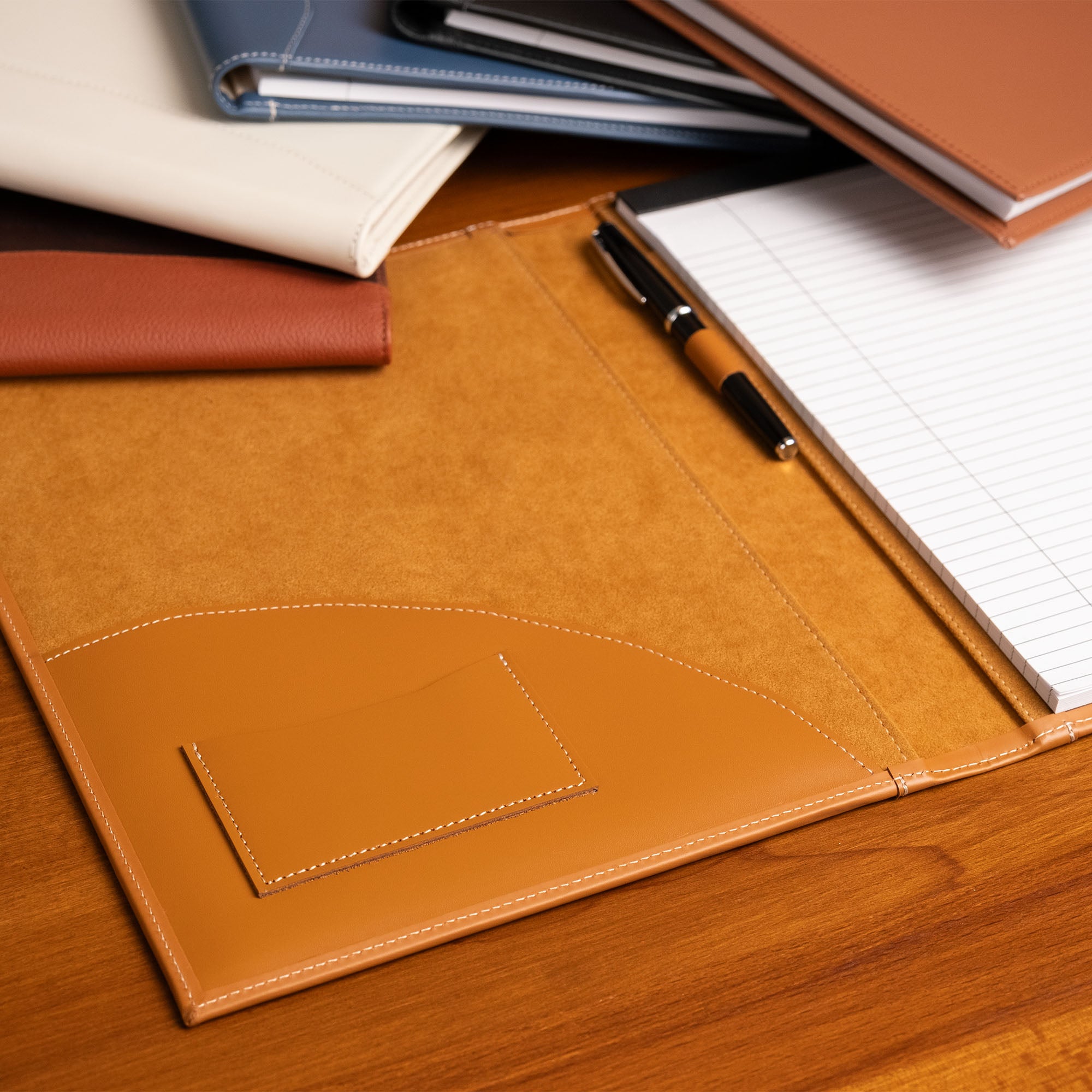 Brown leather folder with notebooks and a pen on a wooden surface