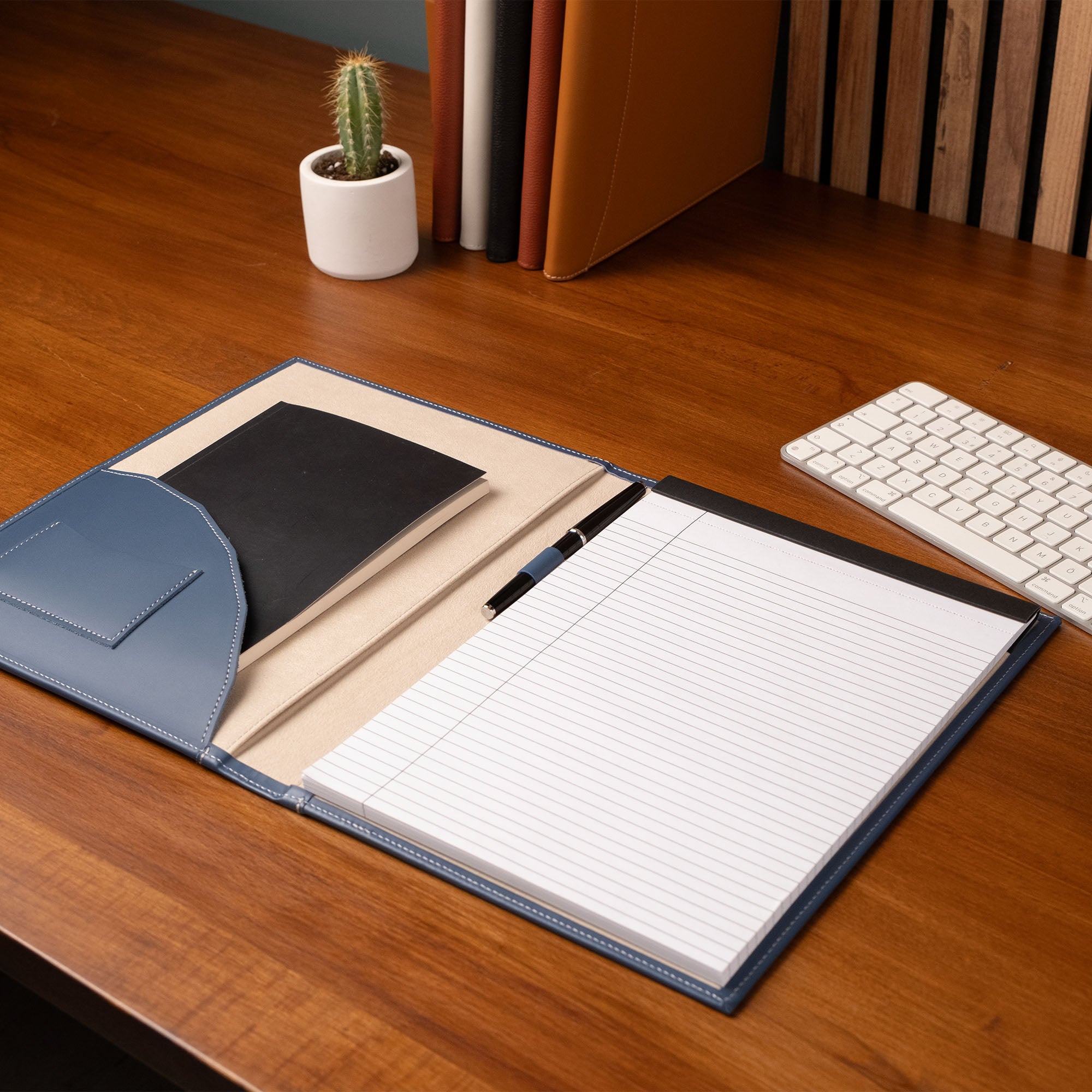 Notebook on a desk with a pen, keyboard, and cactus in the background